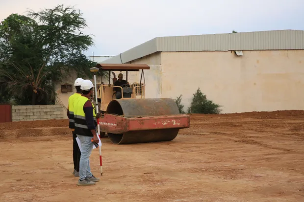 Engineers in high-visibility vests supervising road construction with a roller